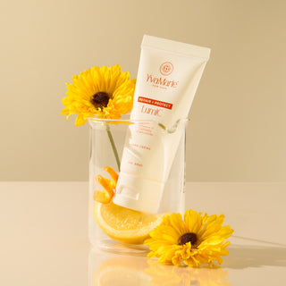 Tube of YvamMarie LumiC on a reflective surface with yellow flowers and a lemon slice.