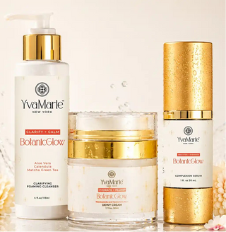 Three Yves Marie skincare products with gold caps and white labels, including a pump bottle, a jar, and a cylindrical container, arranged on a light beige background with decorative water droplets and a small flower.
