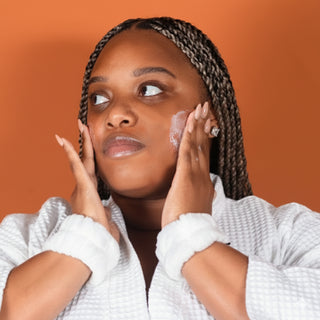 Woman applying YvaMarie cleanser to her face with an orange background