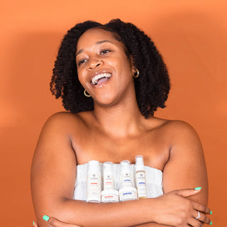 Woman holding YvaMarie skincare products against an orange background